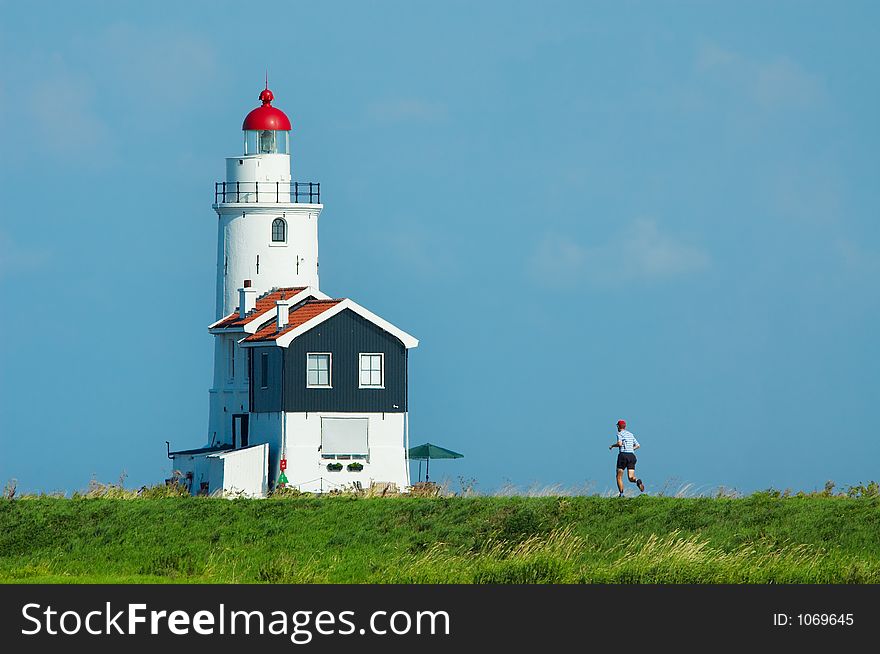 A man jogging towards a lighthouse in summer. A man jogging towards a lighthouse in summer