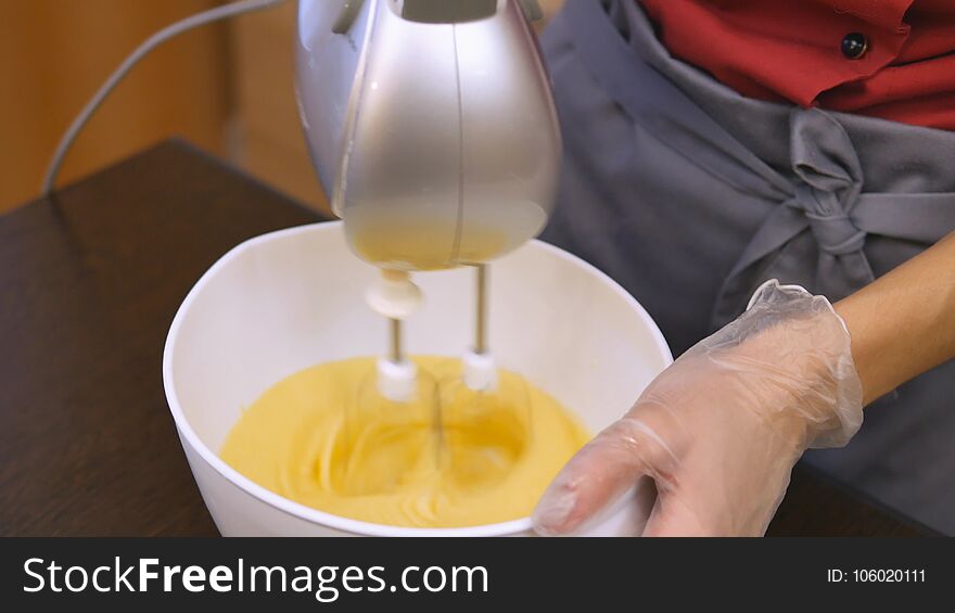 The pastry chef skillfully performs holiday order. A chicken egg is added to the dough. The dough is stirred with a mixer. Woman hand preparing dough and baking a birthday cake. Baking holiday cookies. Christmas and New Year. Magic and dessert for the occasion. The hand of the master in transparent sanitary gloves. 4K 25 h264 Ultra HD