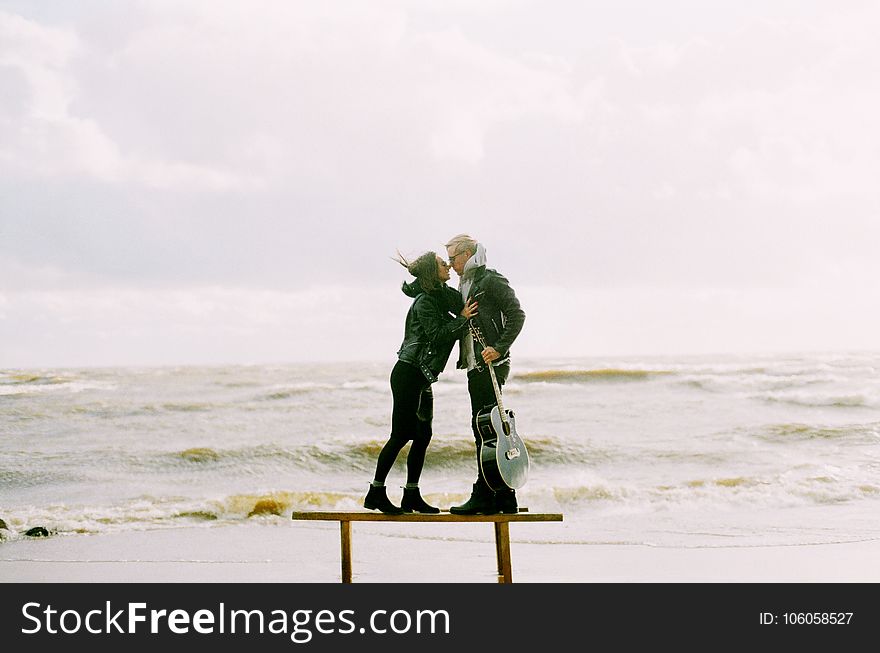 Woman Kissing Man Holding Guitar Beside Beach