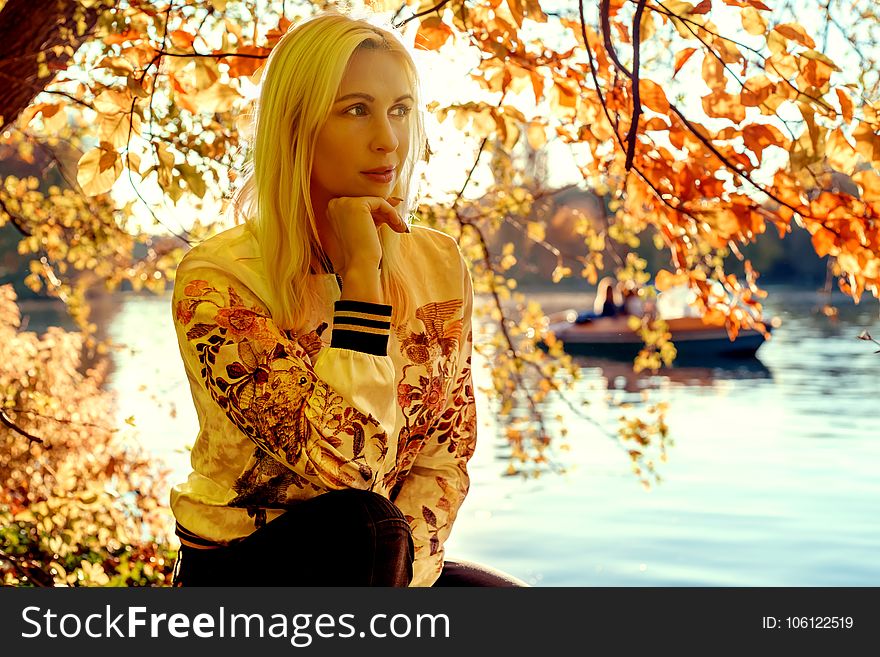 Woman Sitting Under Orange Leaf Tree Near River Bank