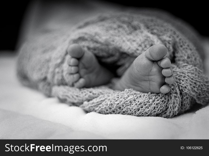 Greyscale Photo Of Human Feet Covered In Knitted Comforter