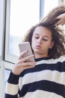 Curly Hair Teen Girl With Mobile Phone By Window Royalty Free Stock Photo