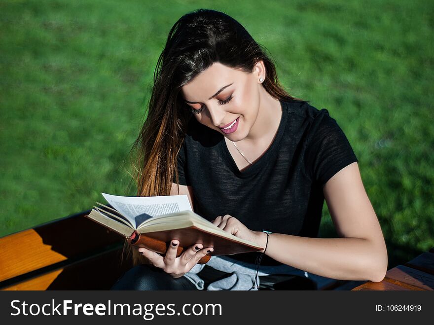 Happy beautiful girl reading a book on sunny spring day on a bench in nature