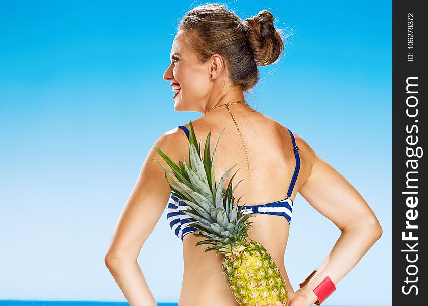 Young woman in bikini on seacoast with pineapple