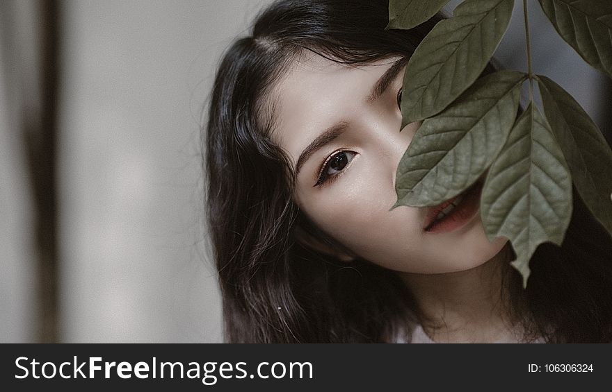Woman With Black Hair Peeking Through Green Leaves