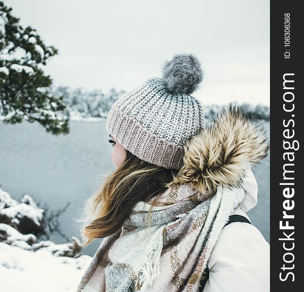 Woman In White And Brown Parka Jacket Wearing Grey Knitted Bobble Hat Near Blue Sea Under White Sky