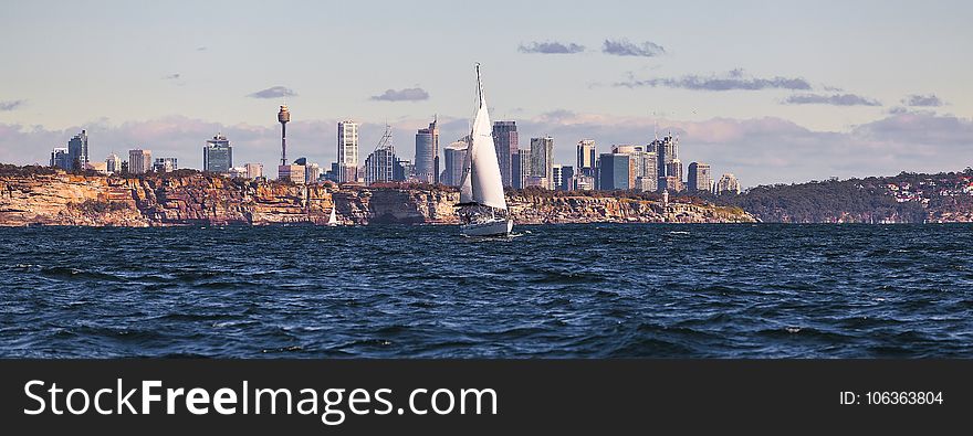 White Sailboat On Body Of Water Near City