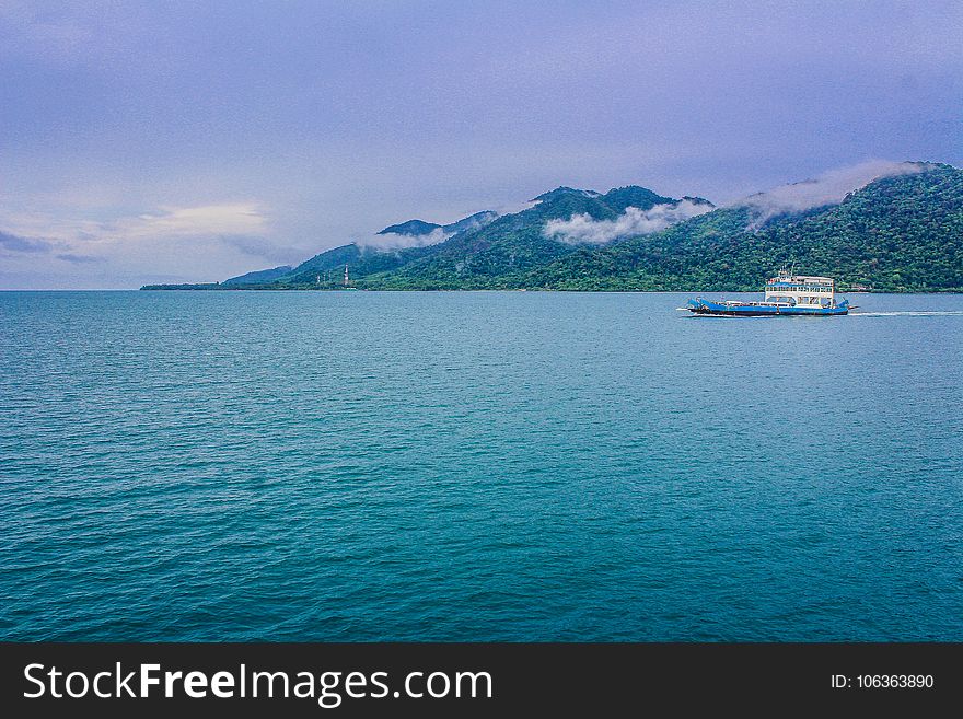 Blue And White Yacht On Teal Sea Near Green Mountain