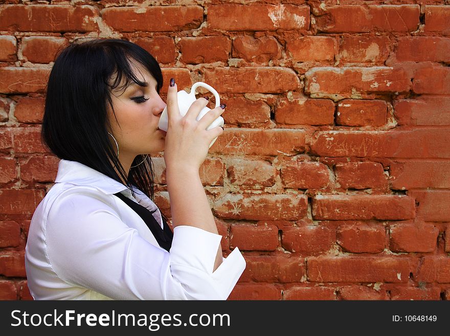 Young woman drinks from a cup on a background of a brick wall. Young woman drinks from a cup on a background of a brick wall
