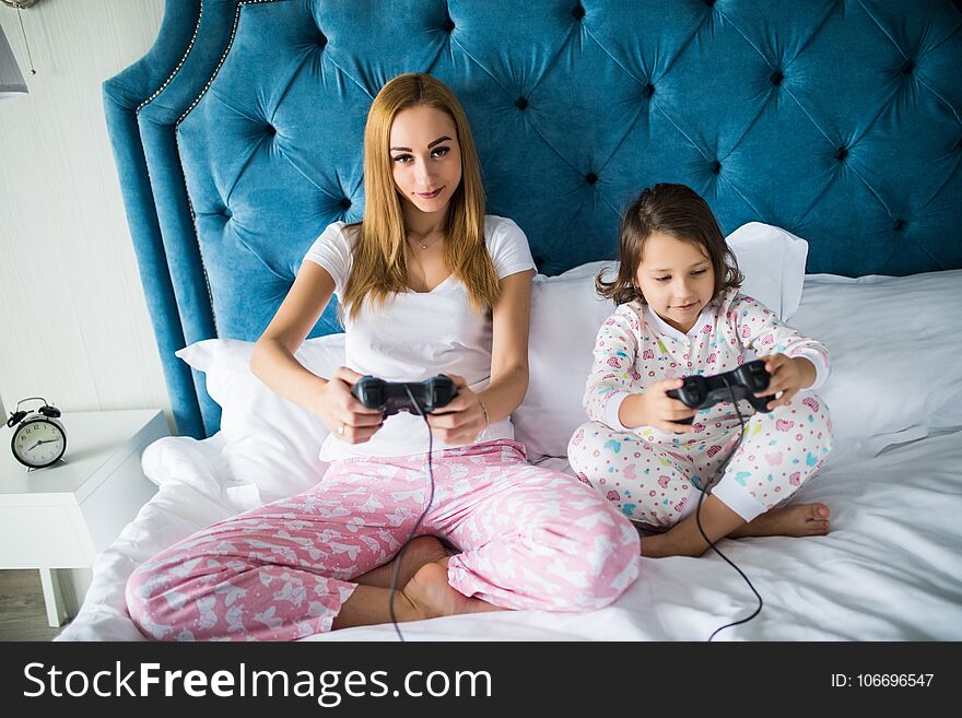 Mother And Little Daughter Plays Game Console Video Games On Bed At Home