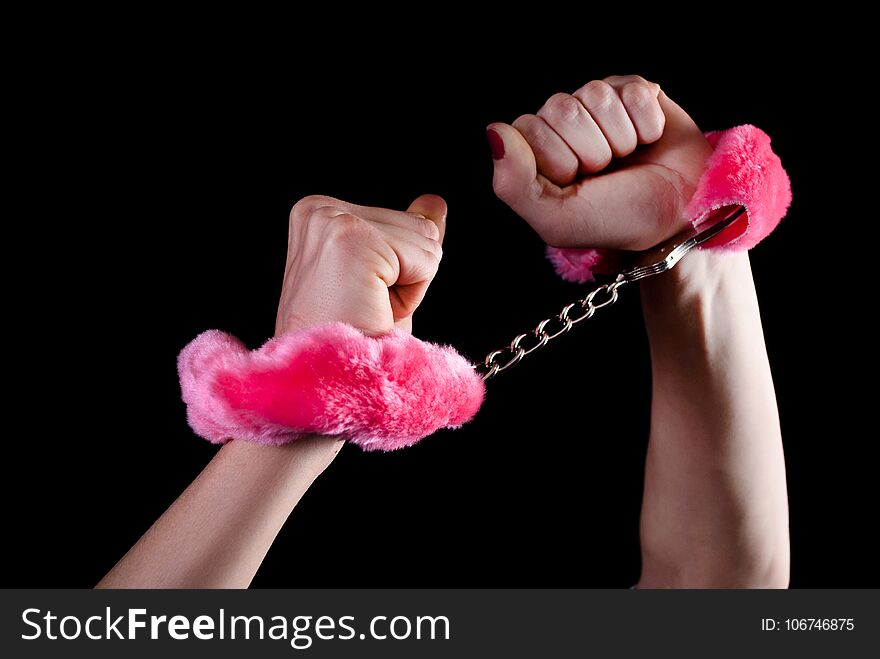 Young women hands in handcuffs with pink fur puffy. Close up. Seductive love concept. Young women hands in handcuffs with pink fur puffy. Close up. Seductive love concept.