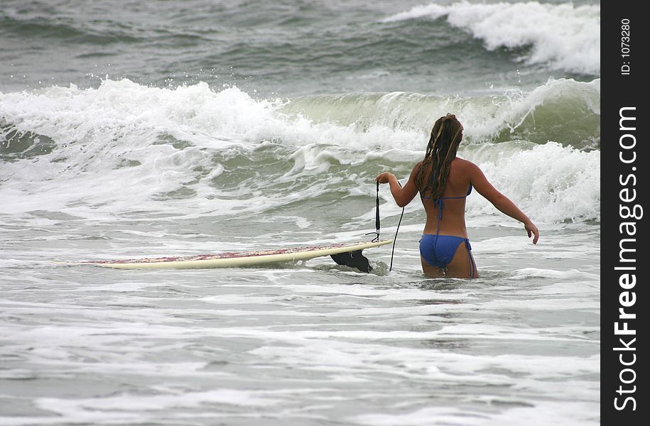 Young girl walking into the ocean dragging a surfboard. Young girl walking into the ocean dragging a surfboard