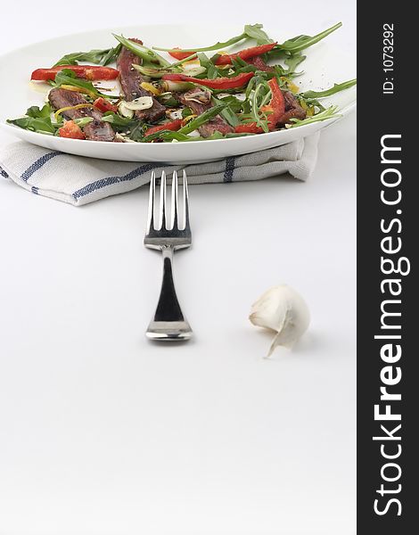 Finely sliced raw bleu beef with rocket and baby capsicum. Baby red capsicum or pepper. Fork aligned with plate. Finely sliced raw bleu beef with rocket and baby capsicum. Baby red capsicum or pepper. Fork aligned with plate.