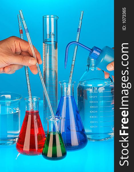 Many different coloured chemical solutions in laboratory glasses with pipettes and two hands on blue background. Many different coloured chemical solutions in laboratory glasses with pipettes and two hands on blue background