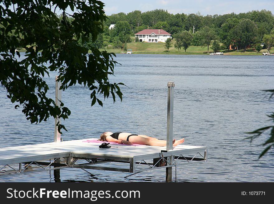 A teen lays out on the dock next to the lake. A teen lays out on the dock next to the lake
