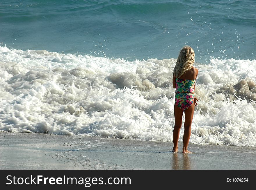 A girl is standing on the sand beach and looking on the waves. A girl is standing on the sand beach and looking on the waves