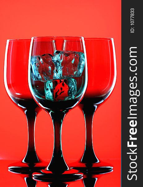 Three glasses and three ice cubes on red background. Three glasses and three ice cubes on red background.