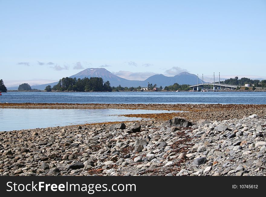 Landscape with beach in foreground and Sitka Alaska bridge and Mt. Edgecumbe volcano in background. Landscape with beach in foreground and Sitka Alaska bridge and Mt. Edgecumbe volcano in background.