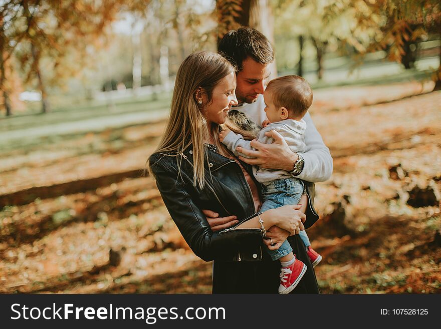 Happy young parents with baby boy in autumn park