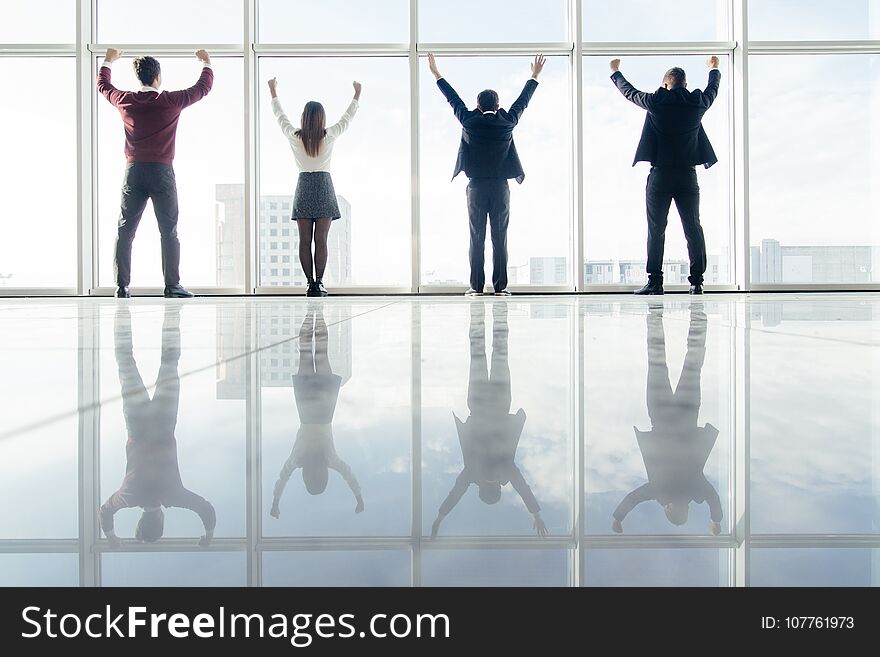 Successful group of business people in office in front of sunshine lit window with arms wide open celebrate victory. Welcoming new