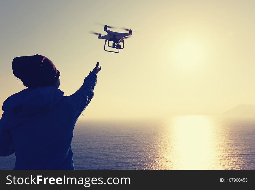 Woman remote controlling a flying drone which taking photo over sunrise sea