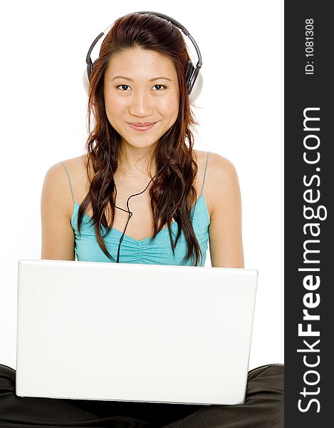 A smiling young asian woman llistens to music from her laptop. A smiling young asian woman llistens to music from her laptop