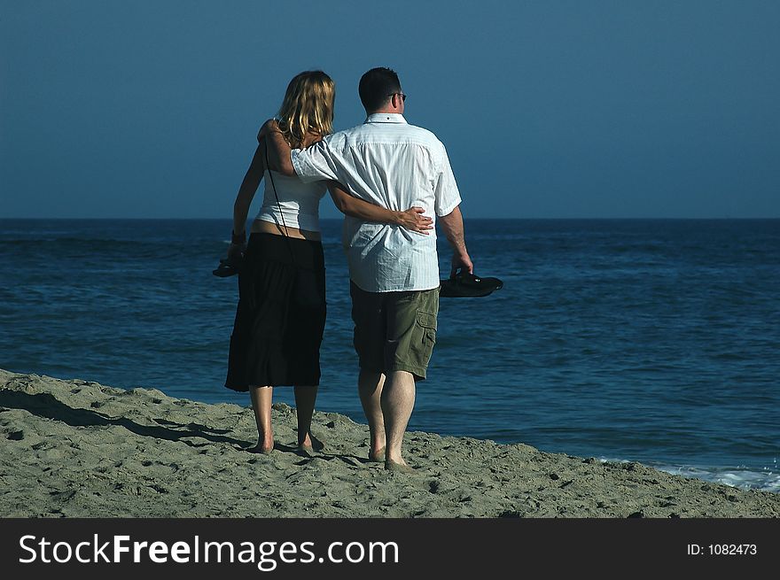 A couple is walking on the beach with sandals in their hands. A couple is walking on the beach with sandals in their hands