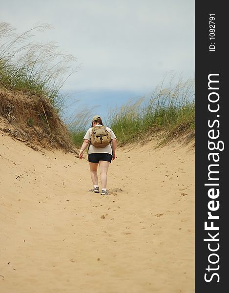 A woman climbing to the top of a sand dune.