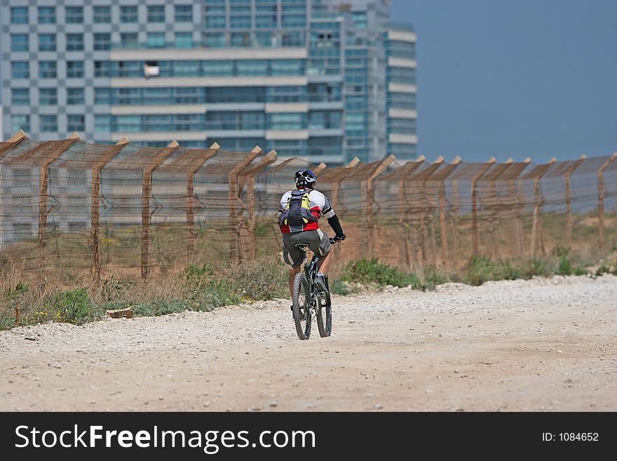 Cyclist riding his bike along a security fence. Cyclist riding his bike along a security fence