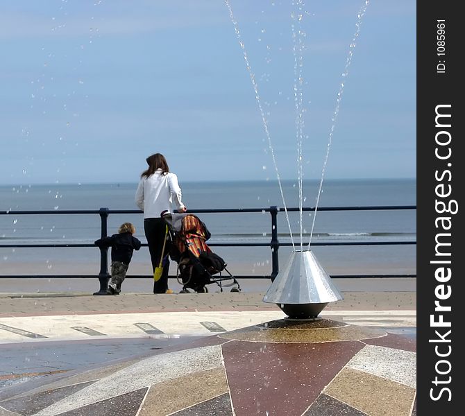 Woman and child look on to beach. Focussed on water in fountain in foreground. Filey, North Yorkshire, UK. Woman and child look on to beach. Focussed on water in fountain in foreground. Filey, North Yorkshire, UK.