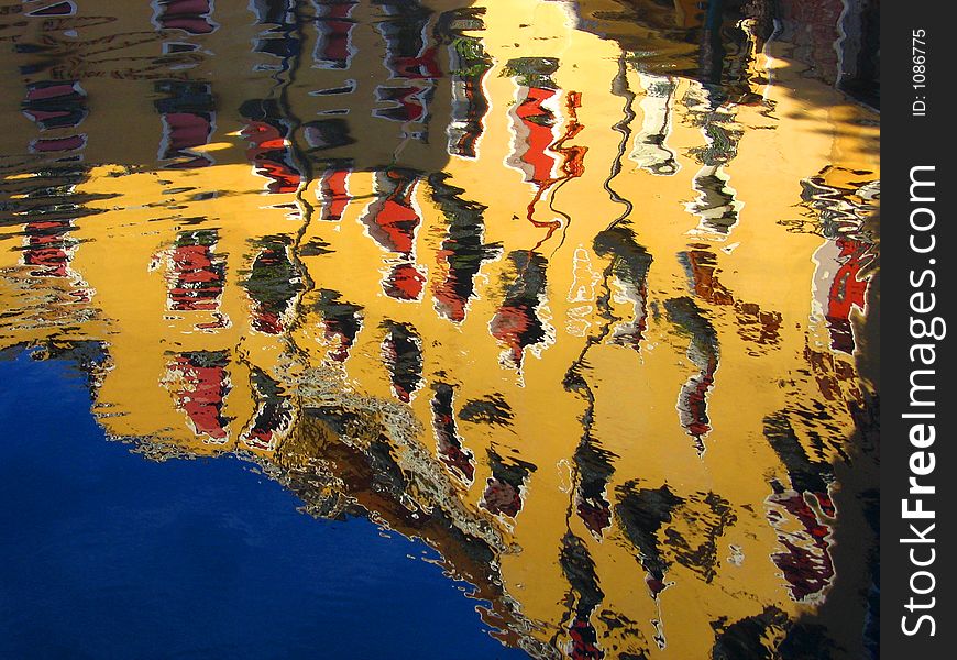 Reflection of yellow building with red window shutters and blue sky on water body. Colours are bright and vivid. Reflection of yellow building with red window shutters and blue sky on water body. Colours are bright and vivid