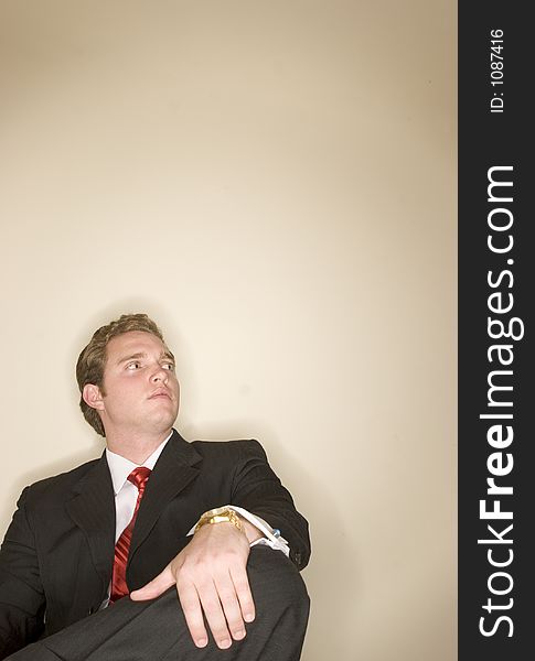 Business man in black suit is holding one leg as he sits crossed legged. Business man in black suit is holding one leg as he sits crossed legged