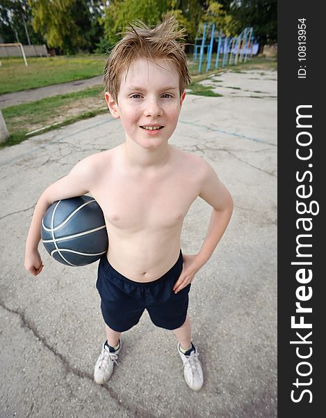 Happy boy plays basketball at school yard, looking at camera