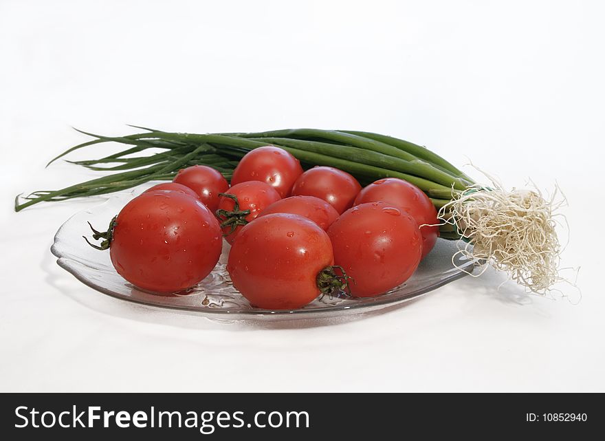 Fresh tomatoes and green salad onion with drops of water in a glass plate prepared for cooking. Fresh tomatoes and green salad onion with drops of water in a glass plate prepared for cooking.