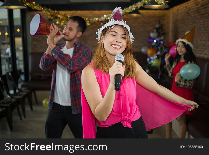 Asian women singer in santa claus hat with a microphone singing and dancing in Christmas party and friend in restaurant. concept of Xmas party, Christmas party and New year party celebration. Asian women singer in santa claus hat with a microphone singing and dancing in Christmas party and friend in restaurant. concept of Xmas party, Christmas party and New year party celebration.