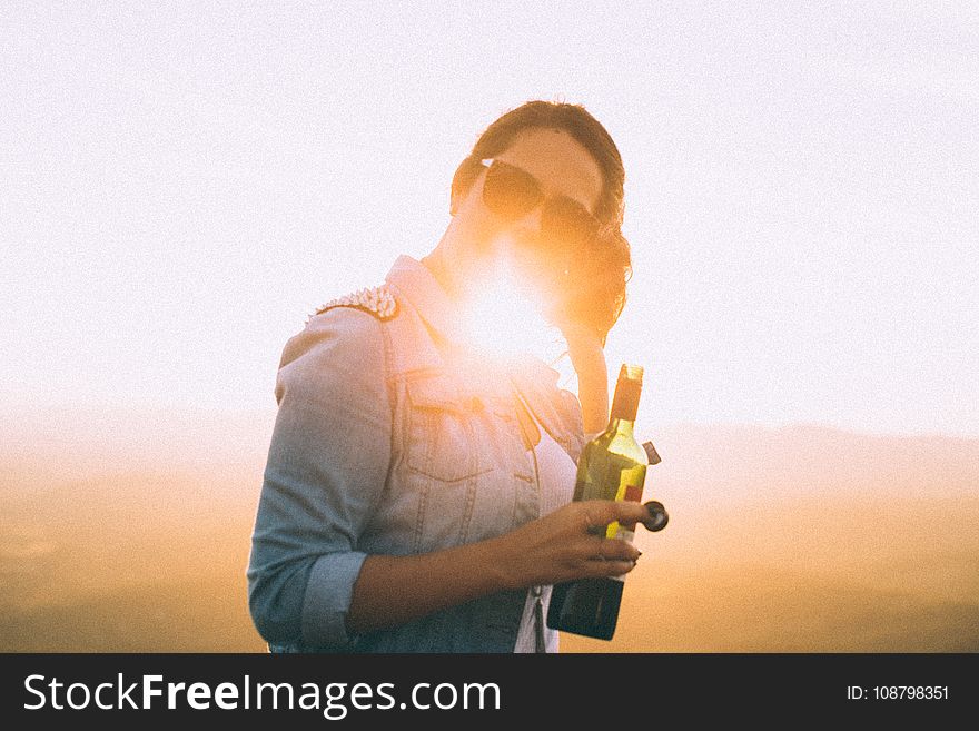 Woman Wearing Blue Denim Jacket Holding Wine Bottle in Golden Hour Photo
