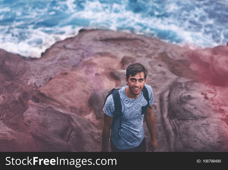 Photo Of Man Wearing Blue Shirt And Backpack Near Ocean