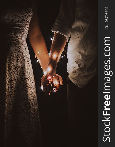 Man and Woman Holding Each Others Hand Wrapped With String Lights