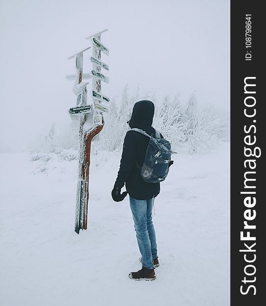 Person Wearing Black Hoodie and Blue Denim Jeans Standing over Frozen Arrow Signage over Snow Ground