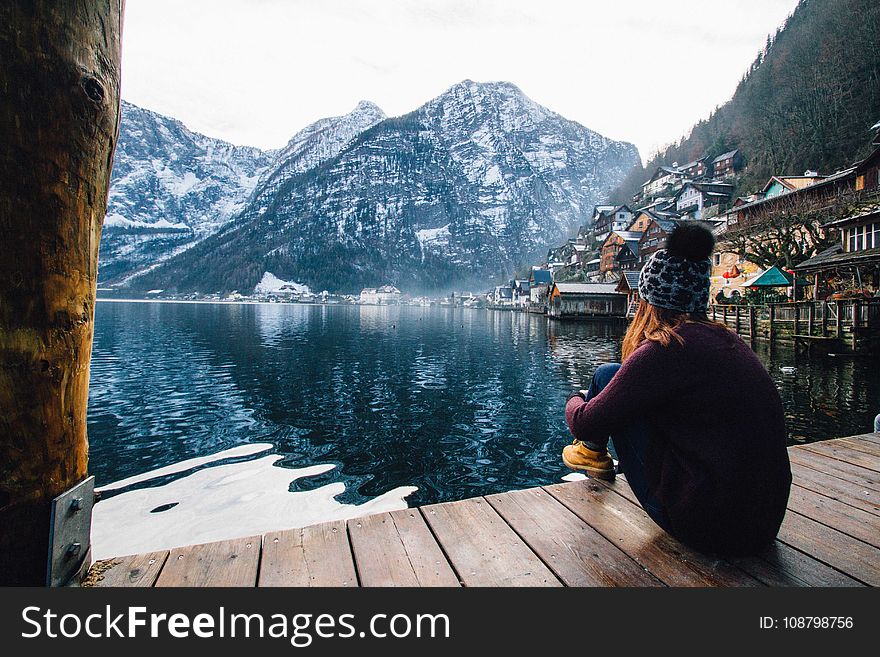 Woman In Purple Sweater Sitting On Wooden Floor With View Of Lake And Mountains