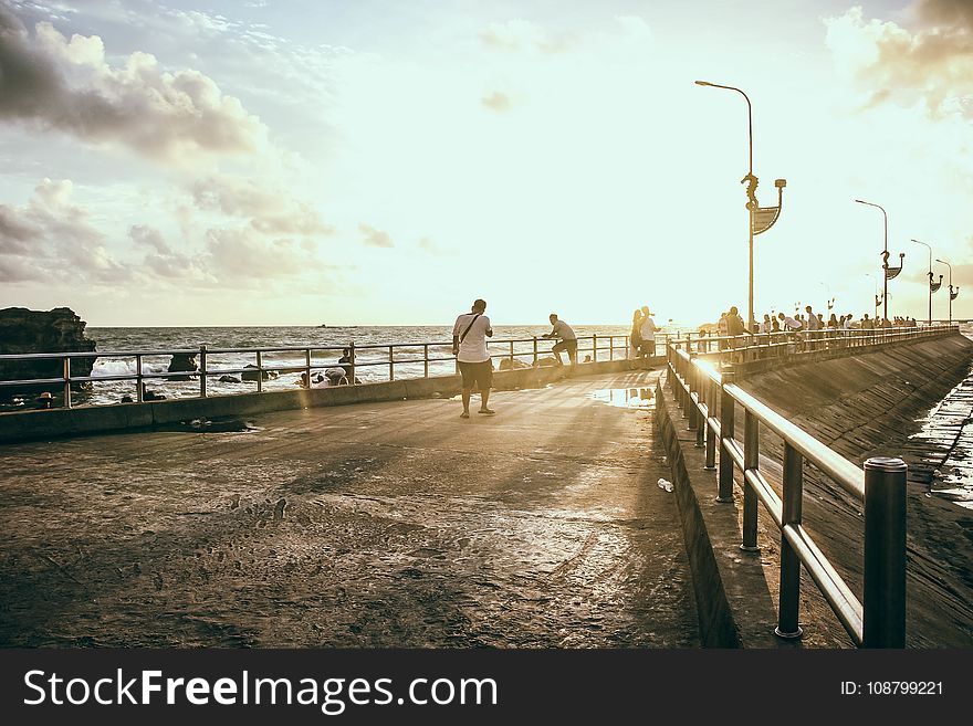 Man Wearing White Shirt Walking on Concrete Pavement Near Sea