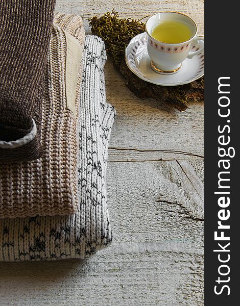 Cozy warm knitted maxi sweaters and cup of tea on wooden background with space for text. Concepts - fashion, comfortable time spent at home, rustic hygge life, relaxing