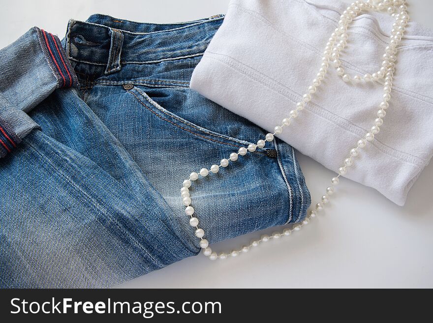 Women`s fashionable casual outfit - blue jeans, white sweater and white pearl necklace, space for text