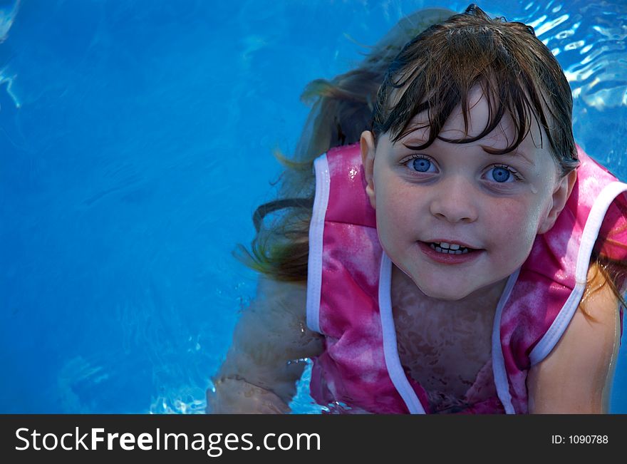 Four year old girl floating in swimming pool; wearing floatation jacket