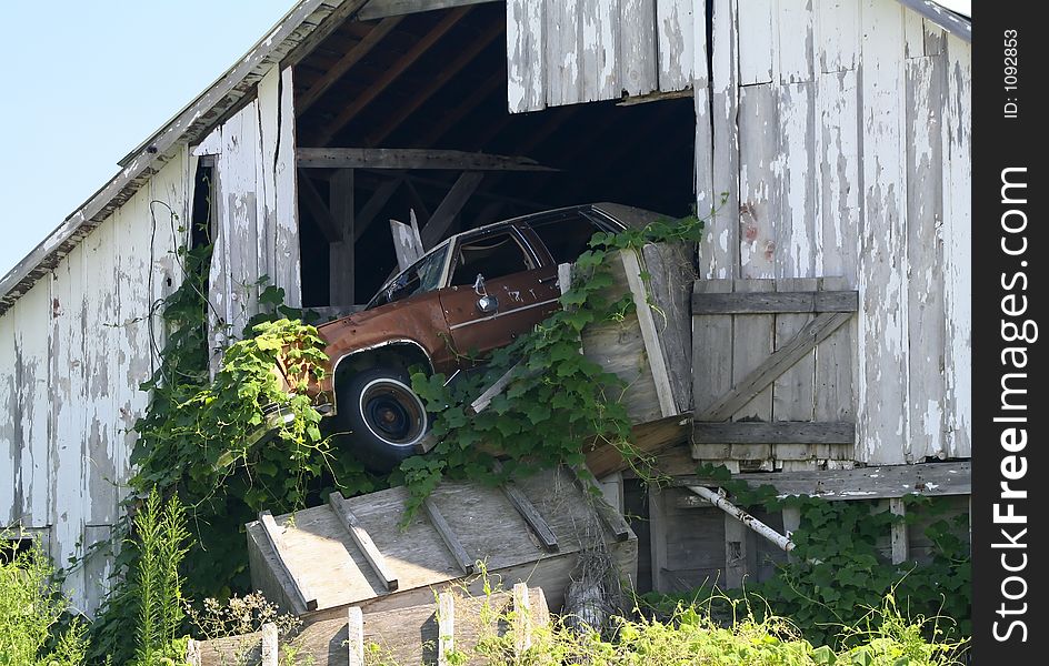 An abandoned car hanging out of an abandoned barn. An abandoned car hanging out of an abandoned barn