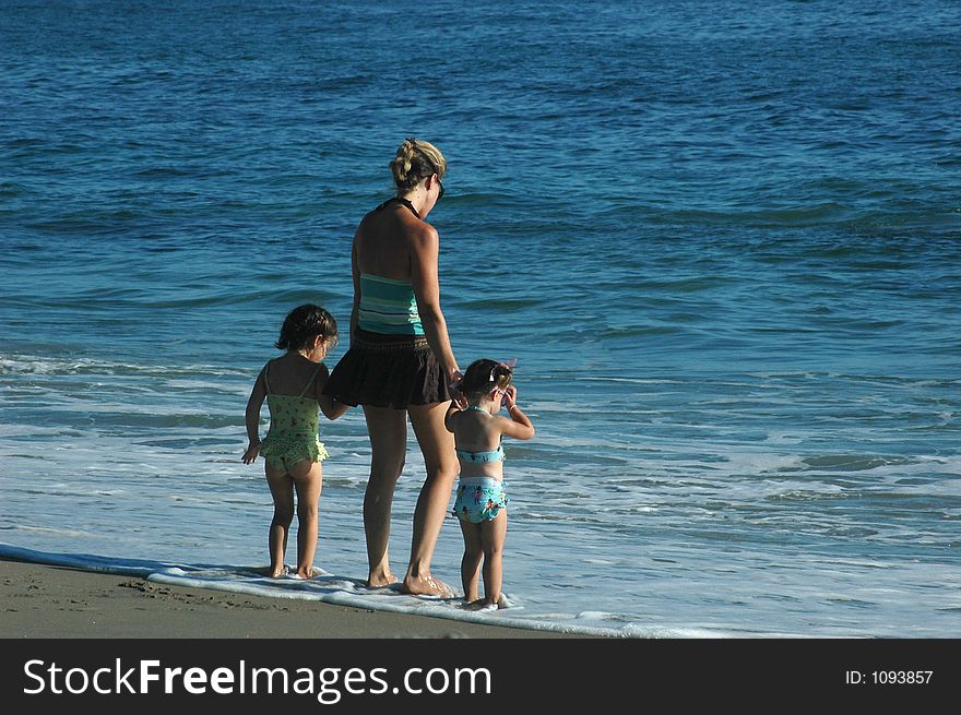 A mom and two daughters standing in the shallow water on the beach. A mom and two daughters standing in the shallow water on the beach