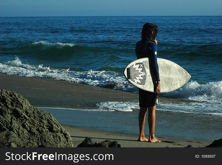 A surfer is standing on the sand beach and waiting for a wave. A surfer is standing on the sand beach and waiting for a wave