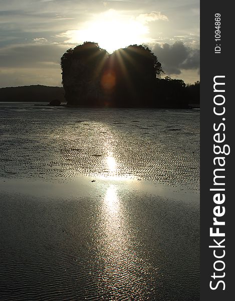 The sun sets behind some limestone rock formations at a beach in Thailand. The sun sets behind some limestone rock formations at a beach in Thailand.