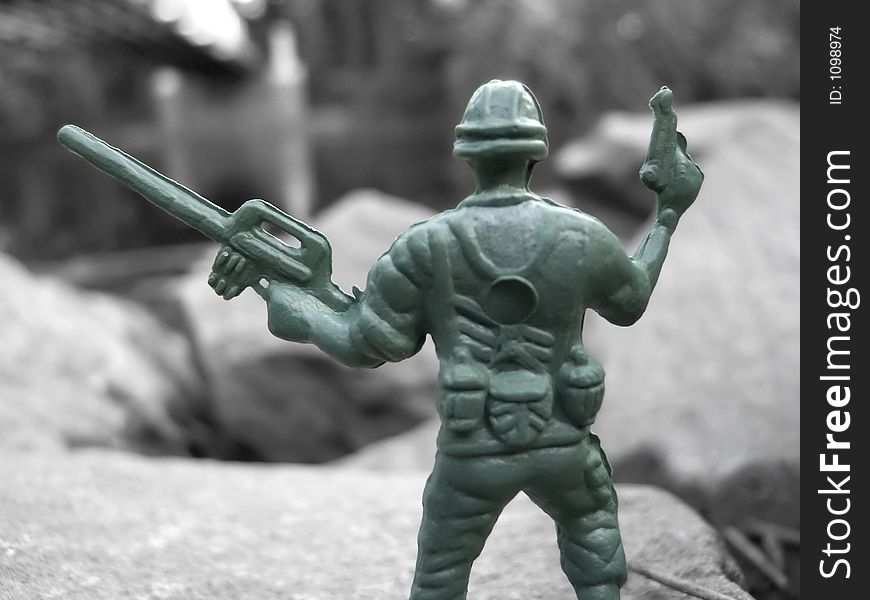 A green plastic army toy soldier in color against a black & white background. A green plastic army toy soldier in color against a black & white background