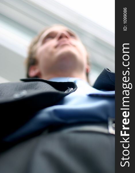 Business man in darker suit, blue shirt, and blue tie is posing in frornt of office building, shot from below. Business man in darker suit, blue shirt, and blue tie is posing in frornt of office building, shot from below